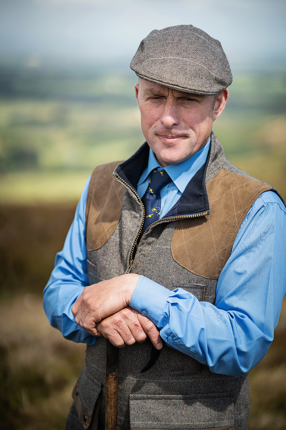 Robbie Douglas-Miller in countryside setting wearing traditional flat cap and shooting vest