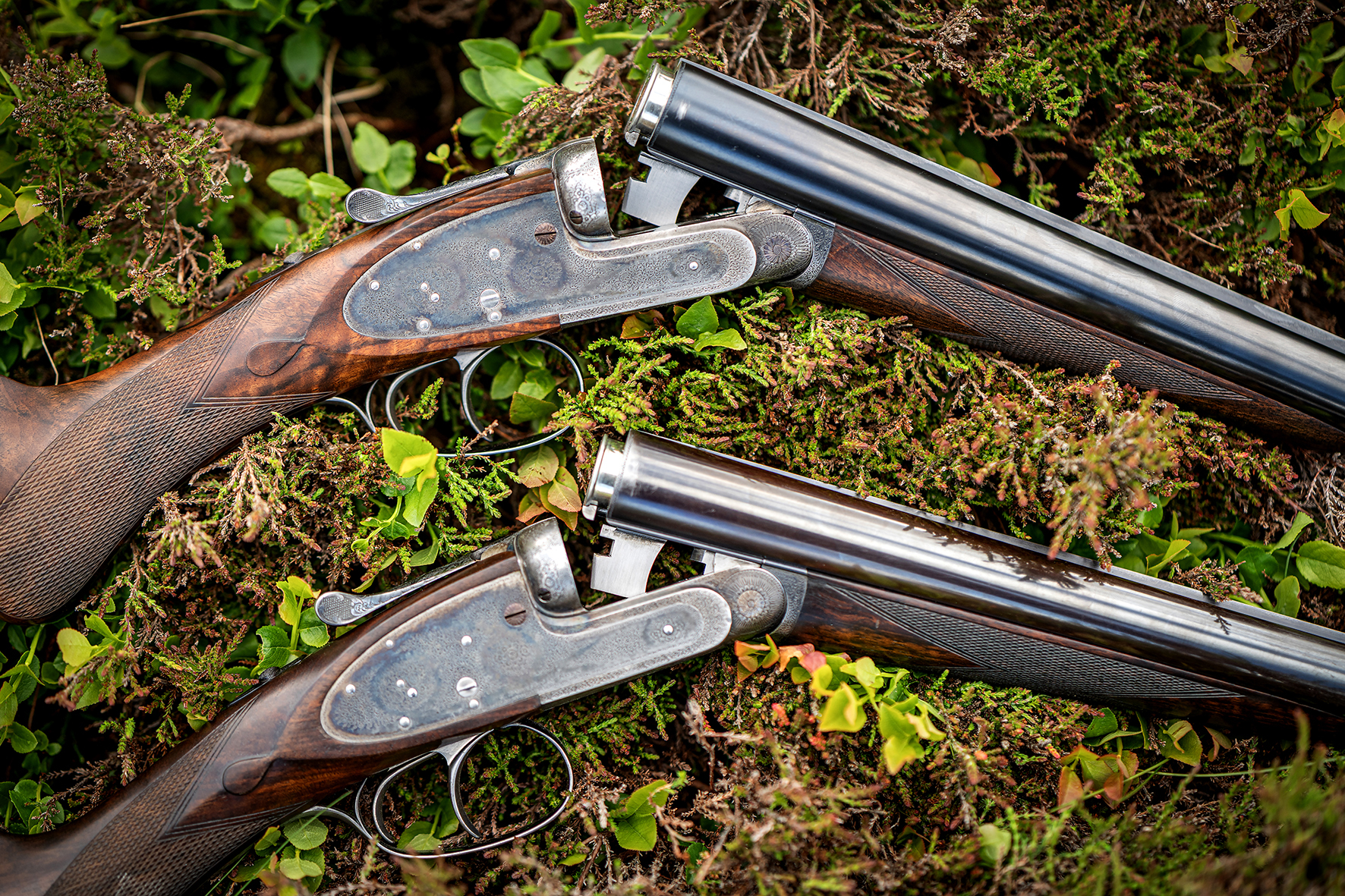 Detail shot of matched pair of traditional side-by-side shotguns on natural ground for Fieldsports Journal editorial